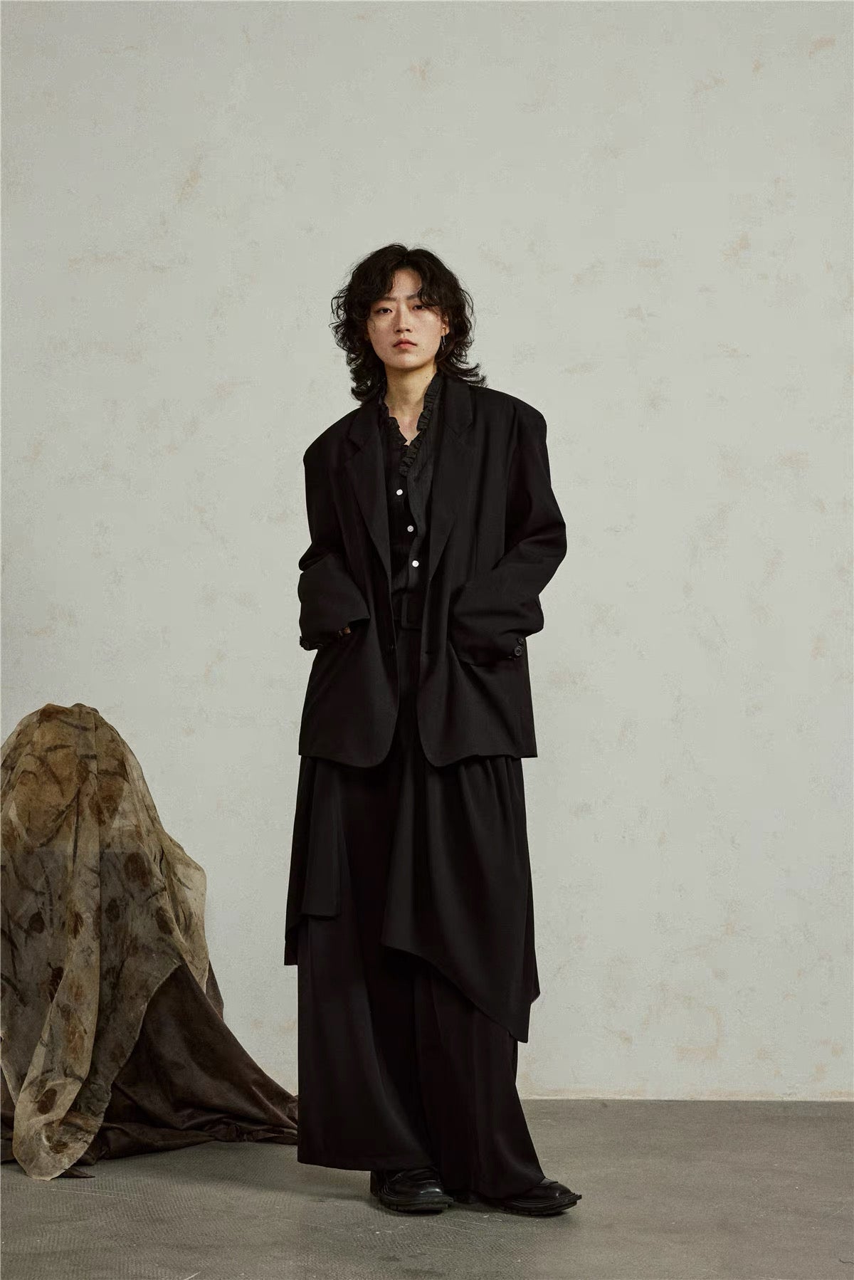 Black draped hem blazer, full-length angled front view with hands in pockets