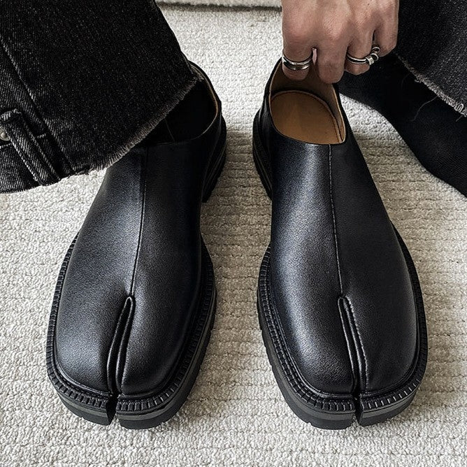 Black leather shoes with unique sole design on a light gray carpet